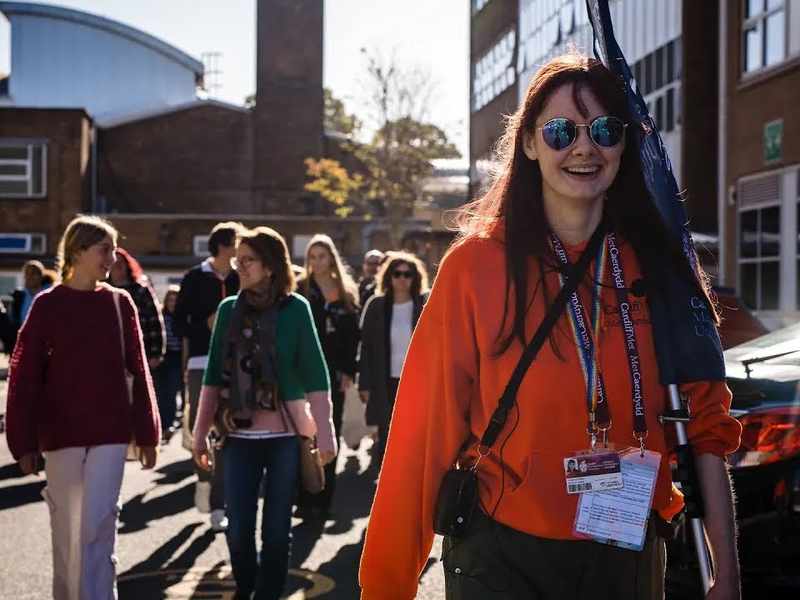 Student ambassador, in bright orange hoodie and sunglasses, leads a tour of the Llandaff Campus