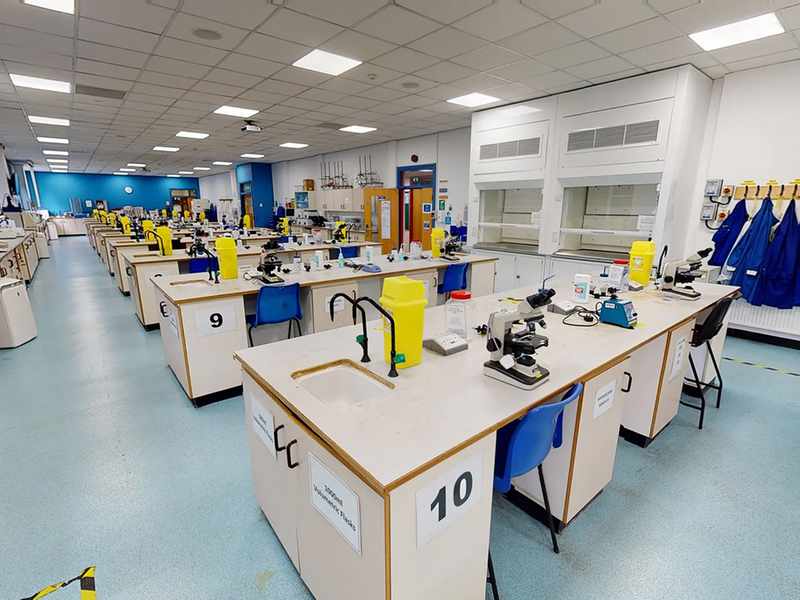 Rows of workbenches in a large laboratory. On the workbenches are microscopes and other scientific equipment.
