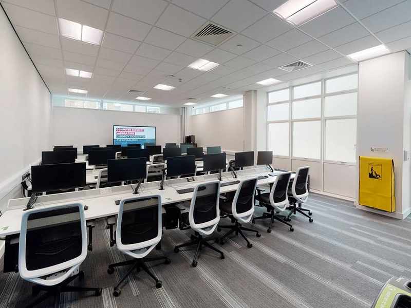Rows of desks with computer screens and desk chairs.