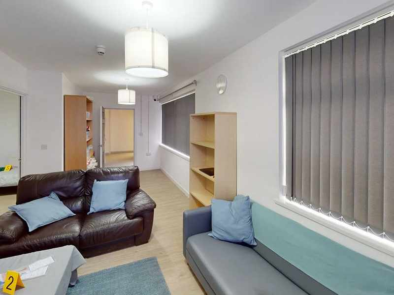 A living room with two sofas and low table. On the table, alongside some pieces of paper, is a small sign with the number two on it.