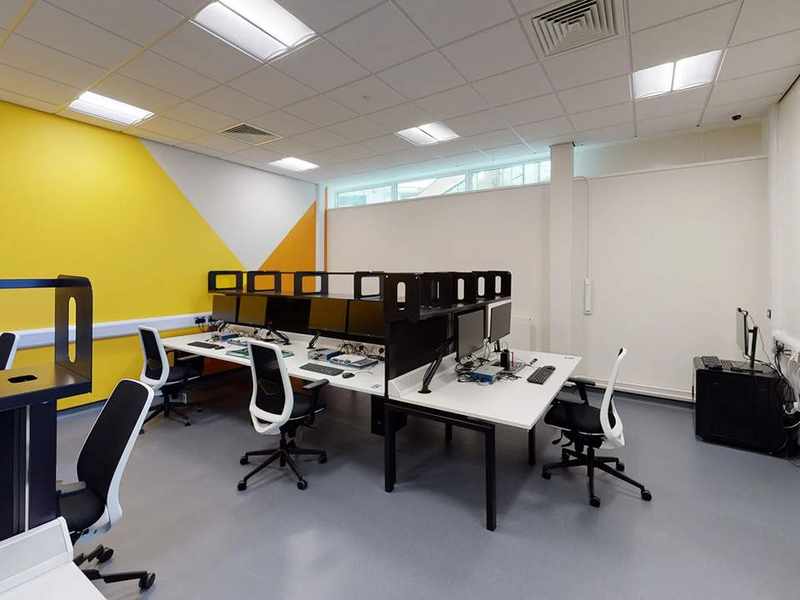 Wide view of computer desks in a bright open room.