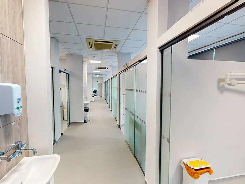 A long brightly lit corridor. Along the right are several small rooms with frosted glass doors.