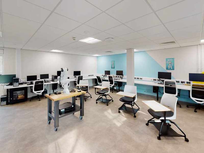 A bright open space with computer desking running along the walls. In the centre of the room is a table with a robotic arm.