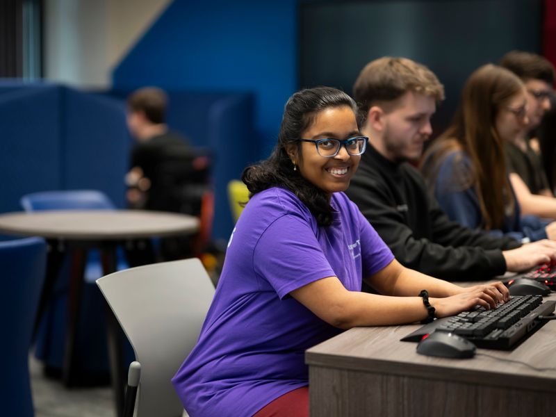 Row of students sat at their computer desks, with the closest smiling at the camera