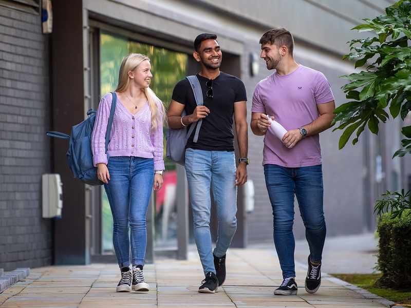 Three students walking together outdoors, smiling and talking.