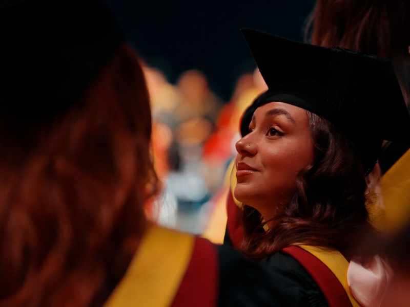 A woman in a graduation gown and cap smiles at the camera, celebrating her academic achievement.