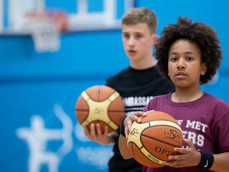Two young boys stand in a gym, each holding a basketball, ready to play and enjoy their time together.