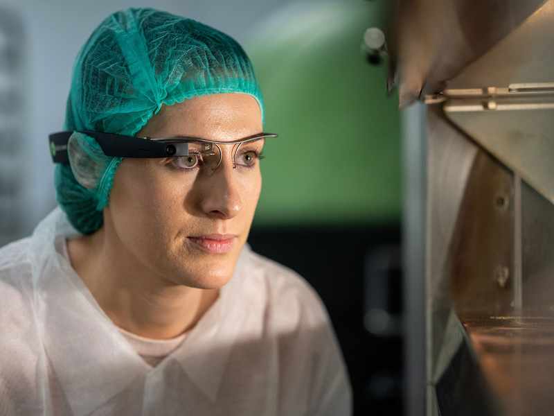 A woman wearing a green hair net, and using a single eye magnifying glass as she works
