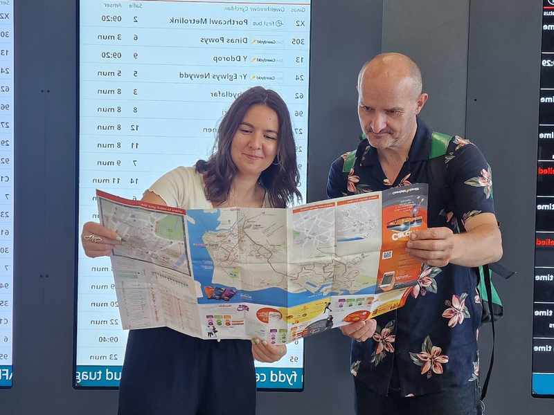 Two individuals inspect a buss map in a busy bus station
