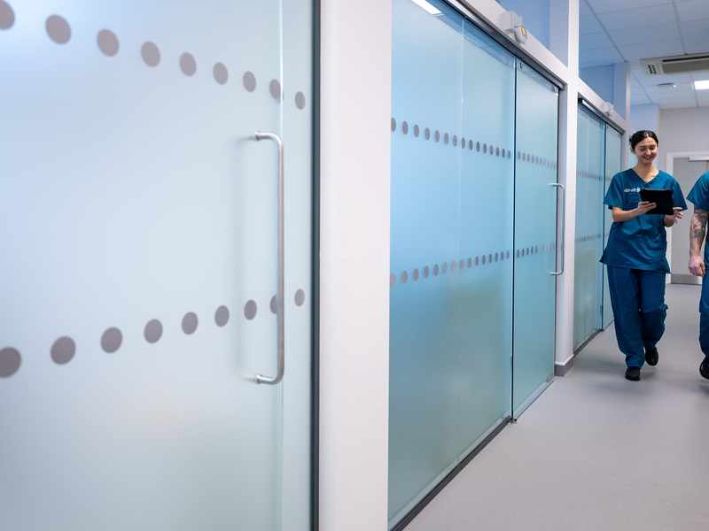 Two young adults in blue nursing scrubs walk through a corridor
