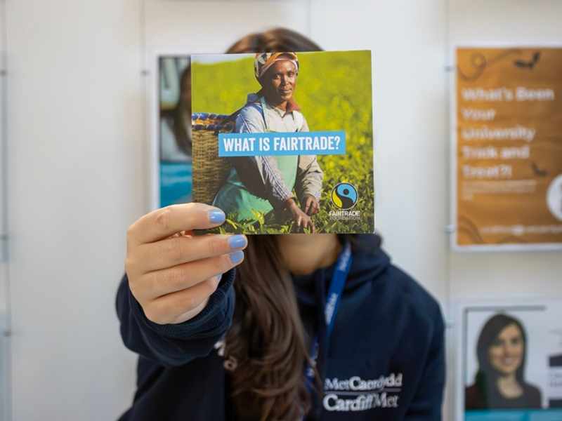 Cardiff Met staff member holds a Fairtrade information leaflet in front of their face