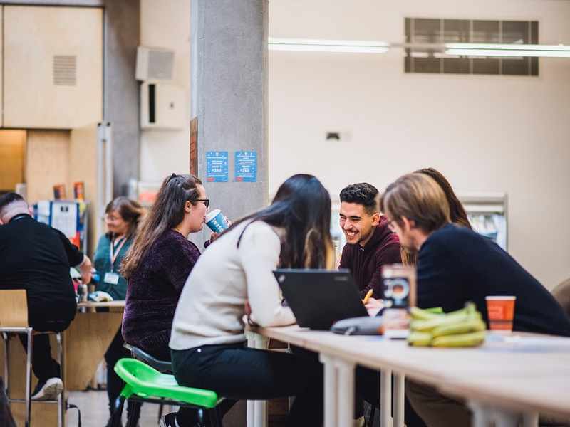 A group of five students sit around a table talking and smiling