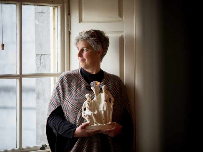 A woman looks out of a window to her right while holding a large white statue with both hands