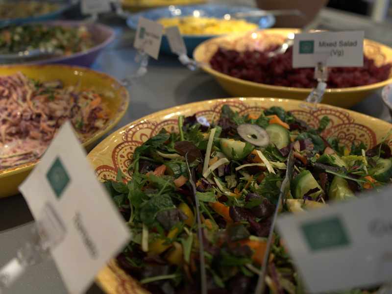 A selection of salads on display in bowls, with accompanying information signs