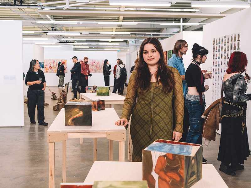 A woman stands in front of an art display, observing the various pieces with interest and contemplation.