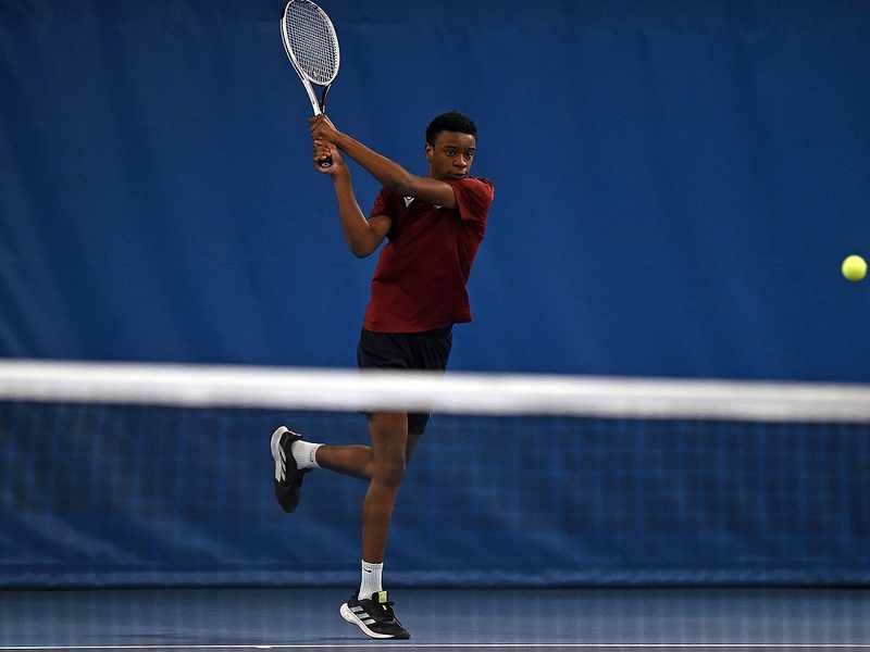 A young man in Cardiff Met exercise t-shirt swings a racket at a tennis ball