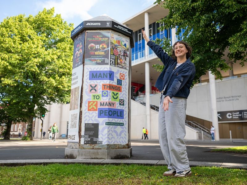 A Cardiff Met student poses next to a poster display stand in the city