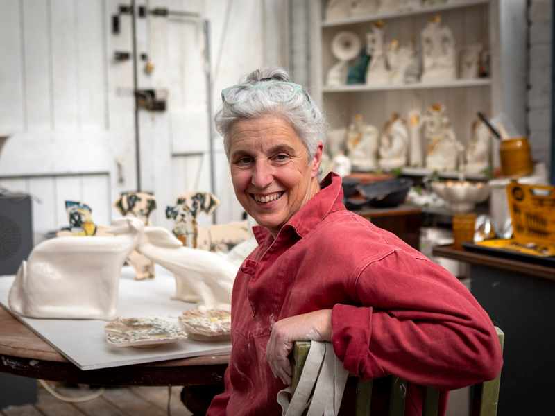 A woman working at a table of ceramics turning around to face the camera