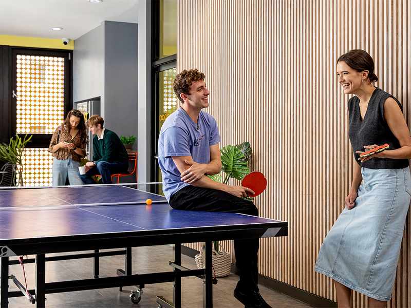 Two individuals playing ping pong in a communal area, showcasing a fun break from studying in a collaborative environment.