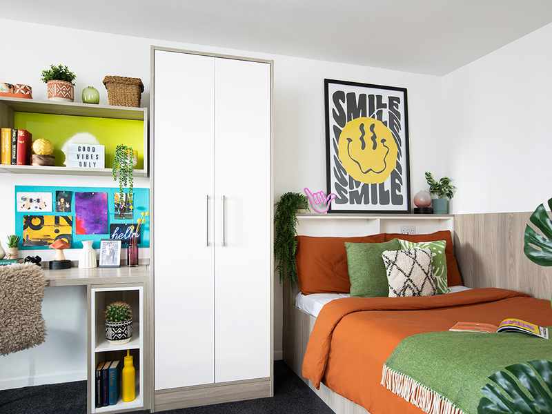 A cozy bedroom featuring a bed, a desk, and a green plant in the corner, creating a serene atmosphere.