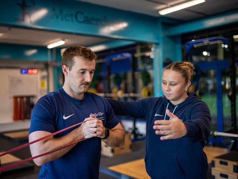 A man and woman exercising in a Cardiff Met Sporty gym, using a resistance band for strength training.
