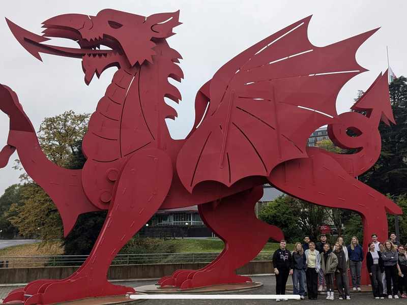 A group of people stand in front of a giant metal red dragon.