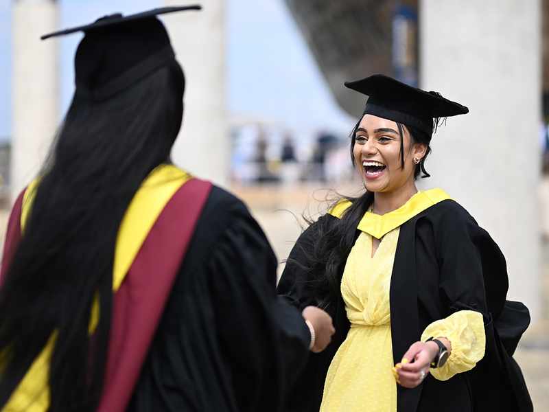 Two women in graduation gowns, celebrating their academic achievements with smiles and camaraderie.