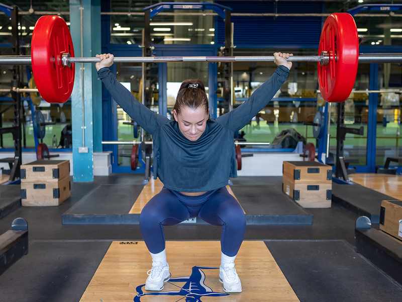 A woman executing a squat in a gym setting, highlighting her commitment to strength training and healthy living.