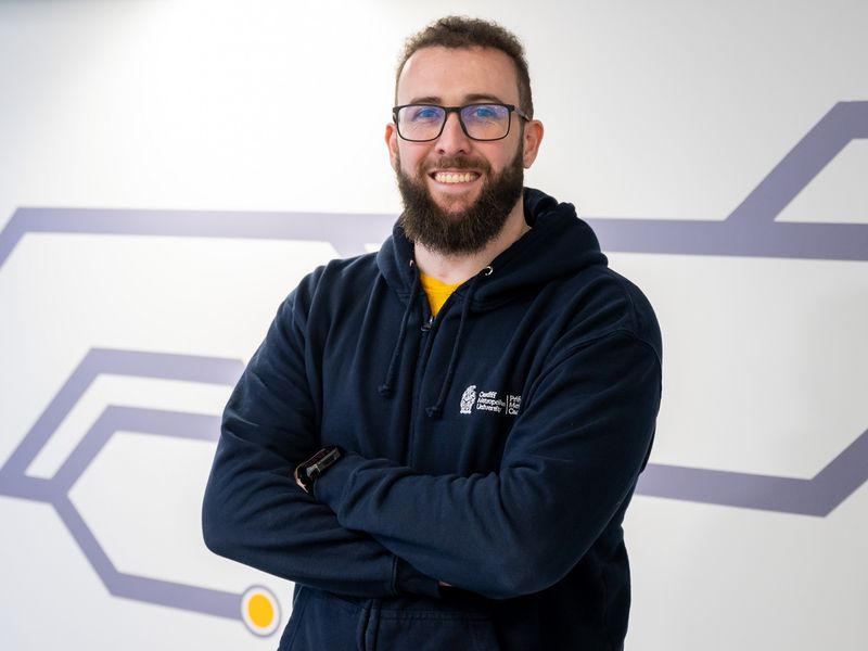 A student coach stands with his arms crossed smiling at the camera