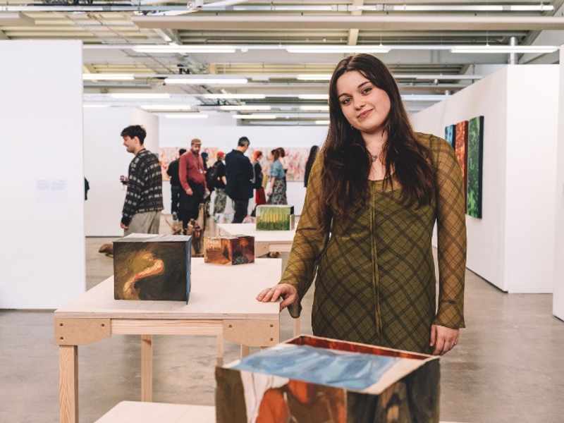 A woman stands in front of an art display, observing the various pieces with interest and contemplation.