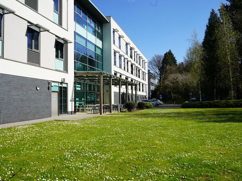 Rear view of the Cardiff School of Management, including an open green space and outdoor seating, on a sunny day