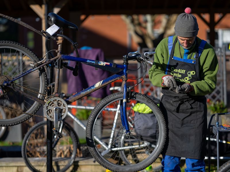 A man inspects a metal bolt in his hands while repairing a bicycle raised on a stand