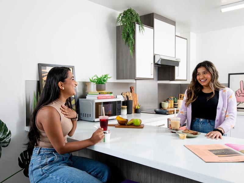 Two young adults sitting and talking at a kitchen island while preparing food