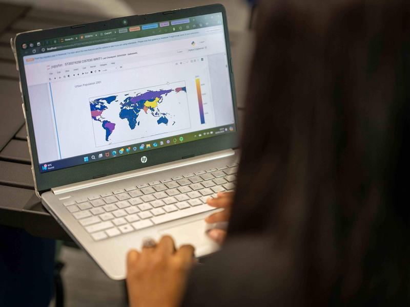 A close-up of a laptop computer. On the laptop screen is a map of the world.
