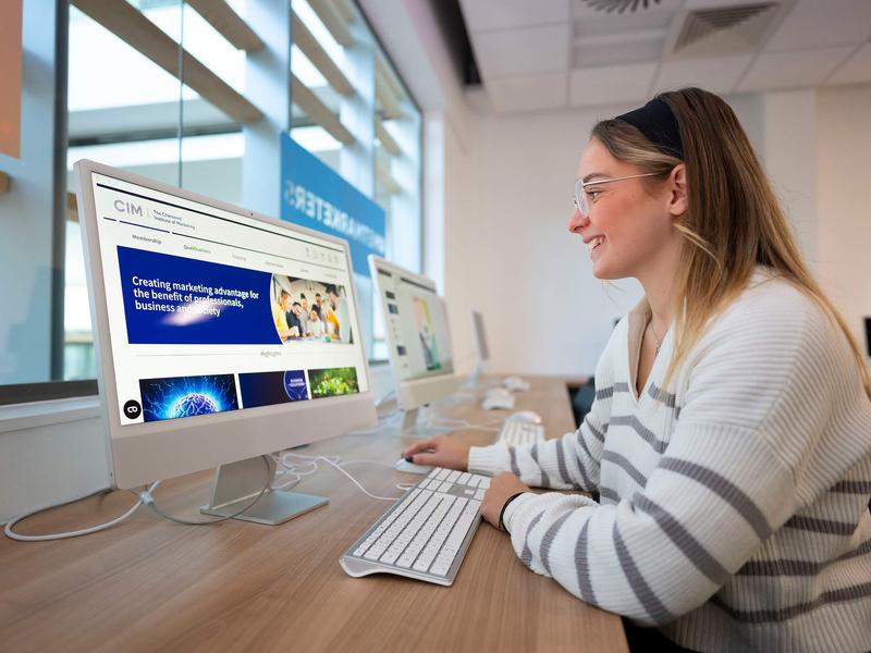 A person sat at a desk in front of a Mac computer.