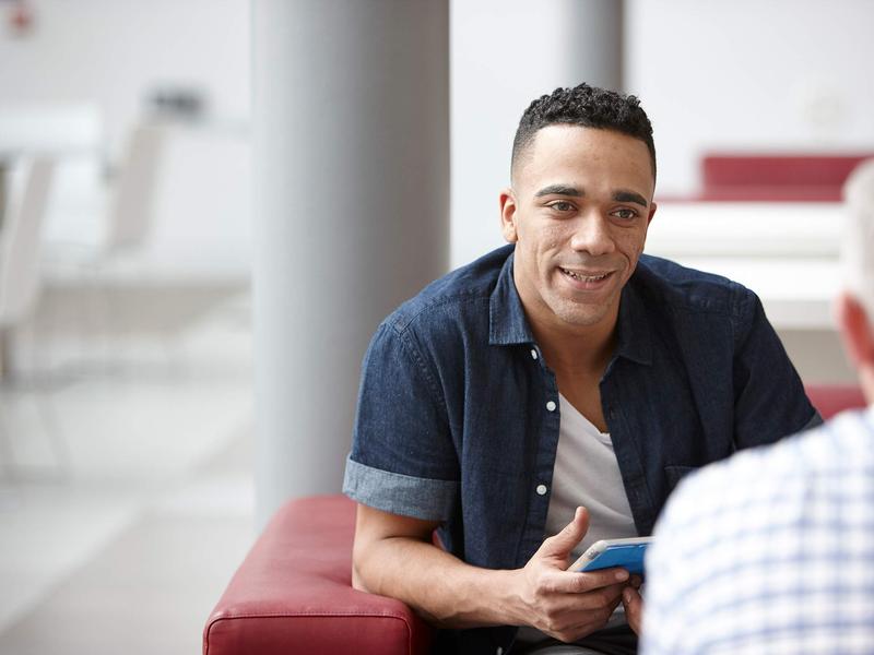 A man holding an iPad while engaged in conversation with another person.