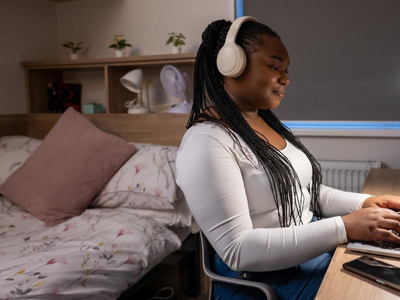 A woman wearing headphones sits at a desk, focused on her laptop, creating a productive work environment.
