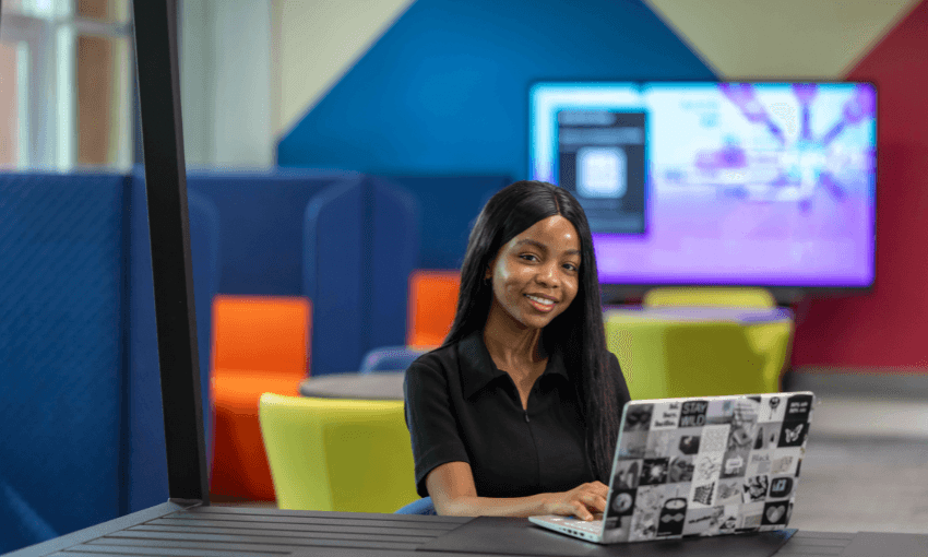 A woman seated at a table, focused on her laptop, engaged in work or study.
