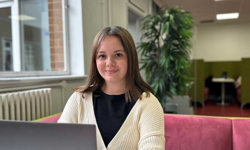 A person sits on a sofa. In front of them is an open laptop computer.