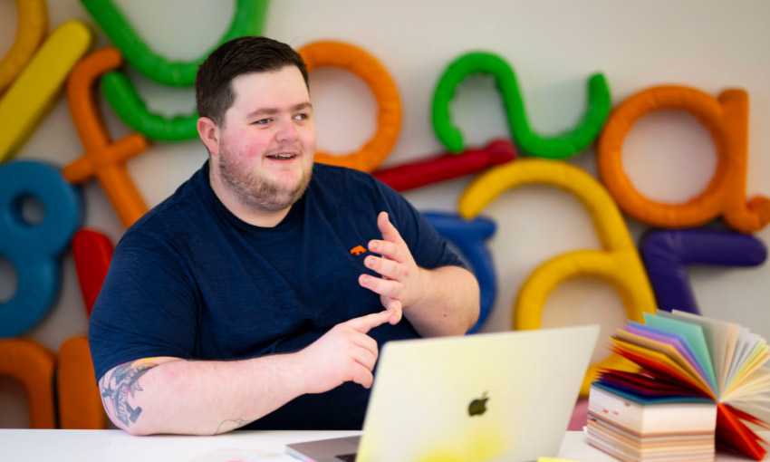 A person sits at a table. In front of them is an open laptop computer.