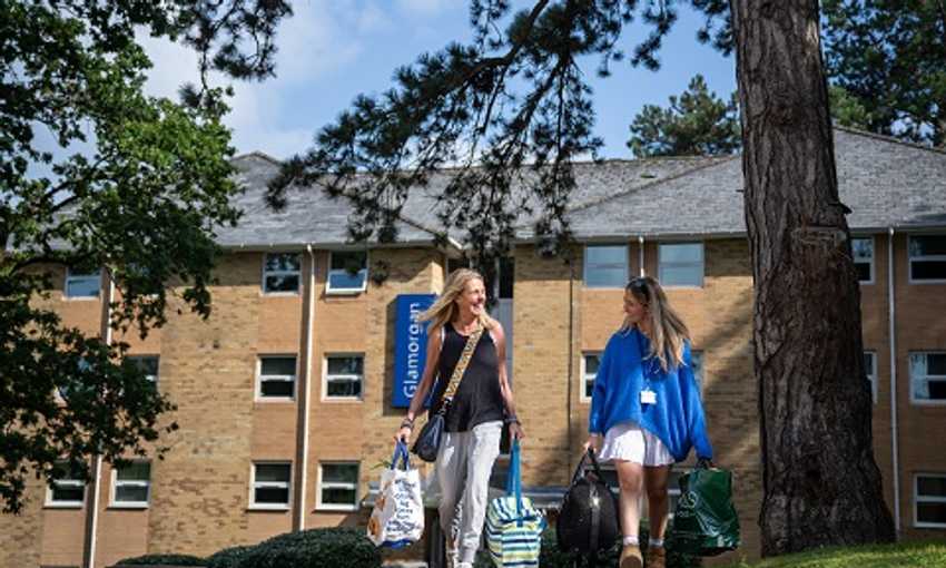 Student and parent carry bags through the Plas Gwyn campus green areas