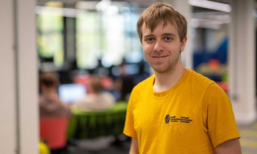 Harrison Heales stands in front of a student workspace