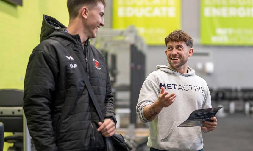 Two men wearing gym gear chatting in the gym, and one has a great hoodie on with Met Active on it.