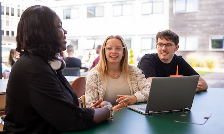 A group of students sit talking at a green table