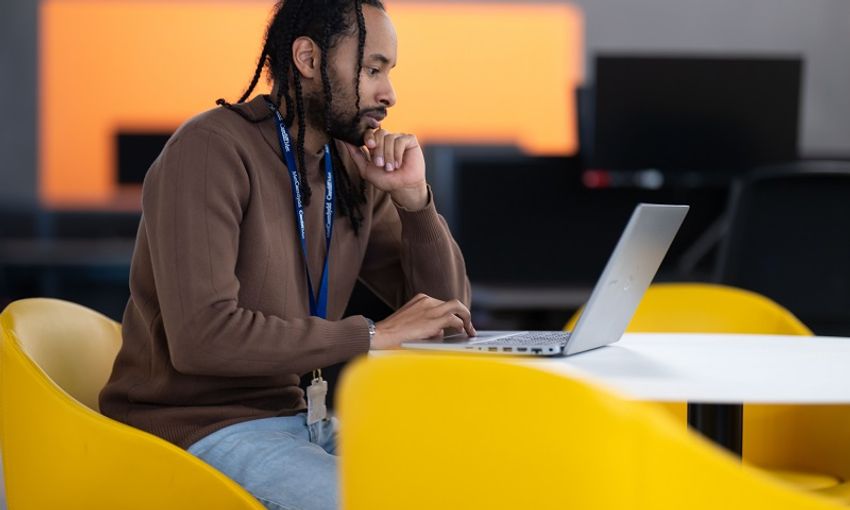 A young man in a brown hoodie works from their laptop
