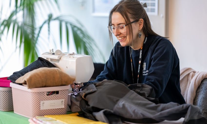 A member of Cardiff Met staff works at a sewing machine to repair clothing
