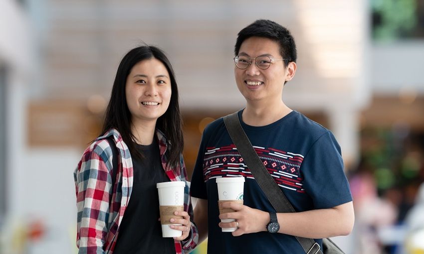 Two young adults holding coffees smile for a photograph