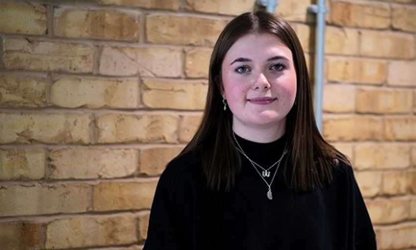 A young woman stands against a rustic brick wall, highlighting her individuality and the urban backdrop.