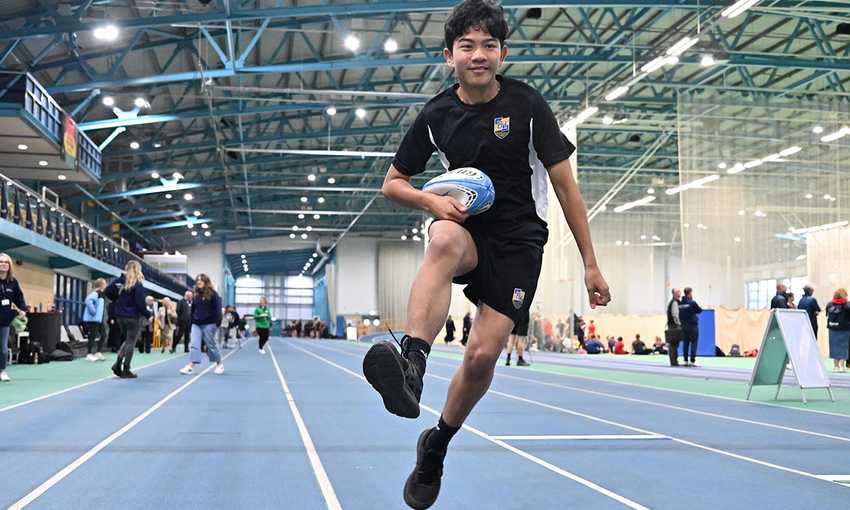 School pupil running with rugby ball on the running track inside the National Indoor Athletics Centre at Cardiff Metropolitan University's Cyncoed campus