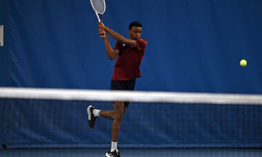 A young man in Cardiff Met exercise t-shirt swings a racket at a tennis ball